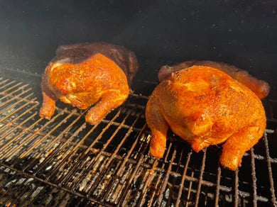 Two whole chickens roasting on a grill with Atomic Chicken charcoal rub