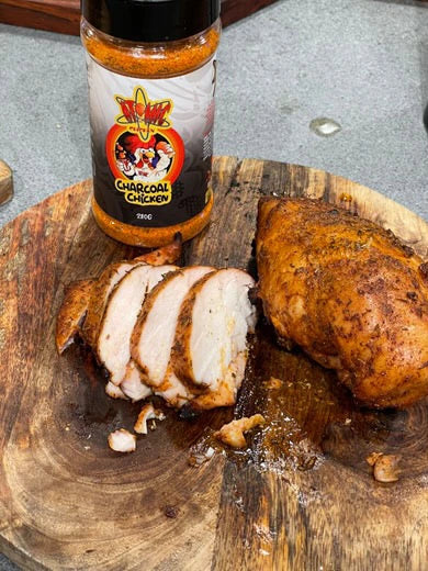 Sliced roast chicken breast with Atomic Chicken charcoal seasoning jar and sauce on a board