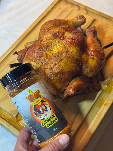 Whole roasted chicken on cutting board with Atomic Chicken charcoal rub held in foreground