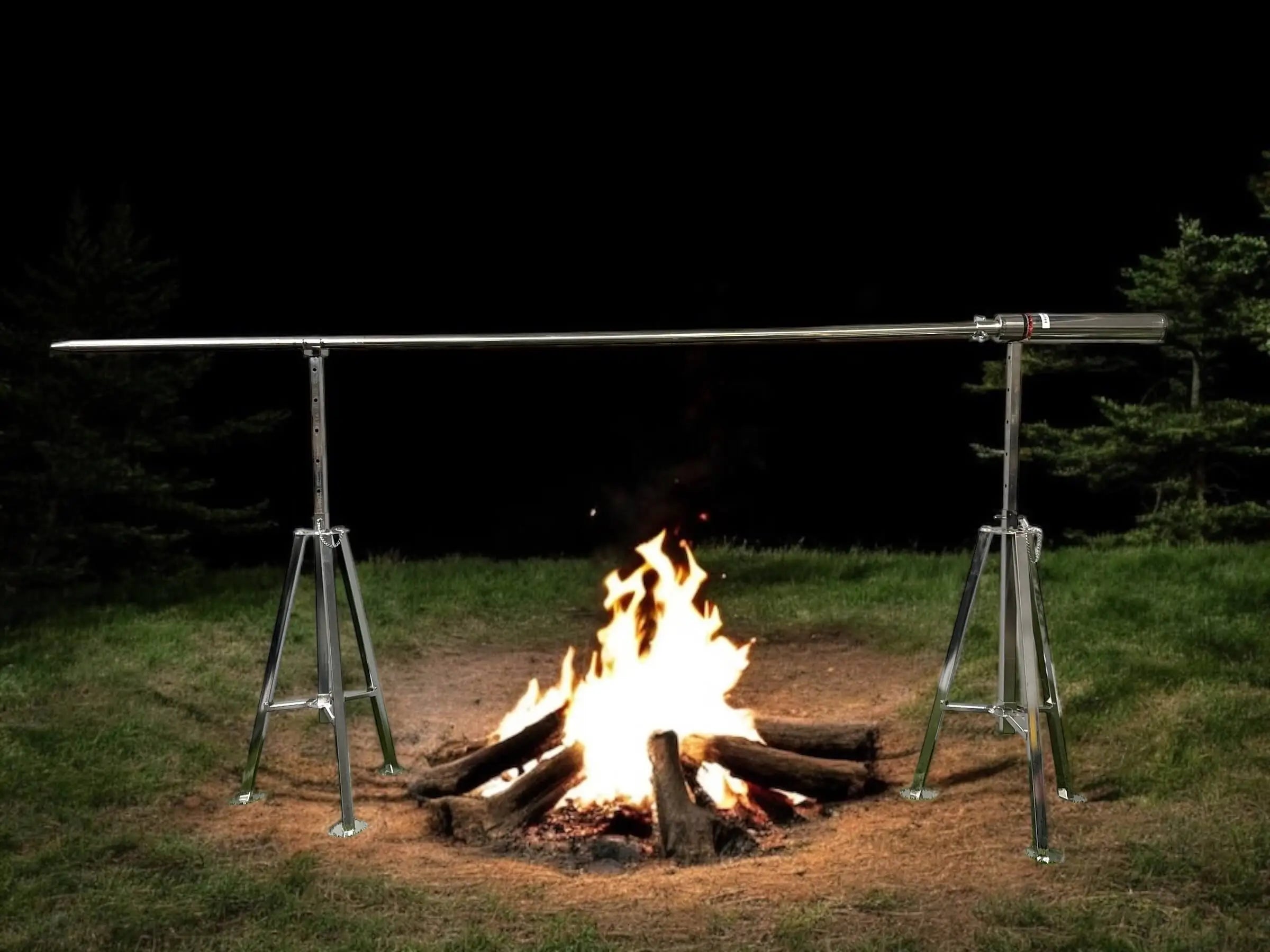 Camping Rotisserie Elite set up over open campfire at night with stainless steel tripod stands