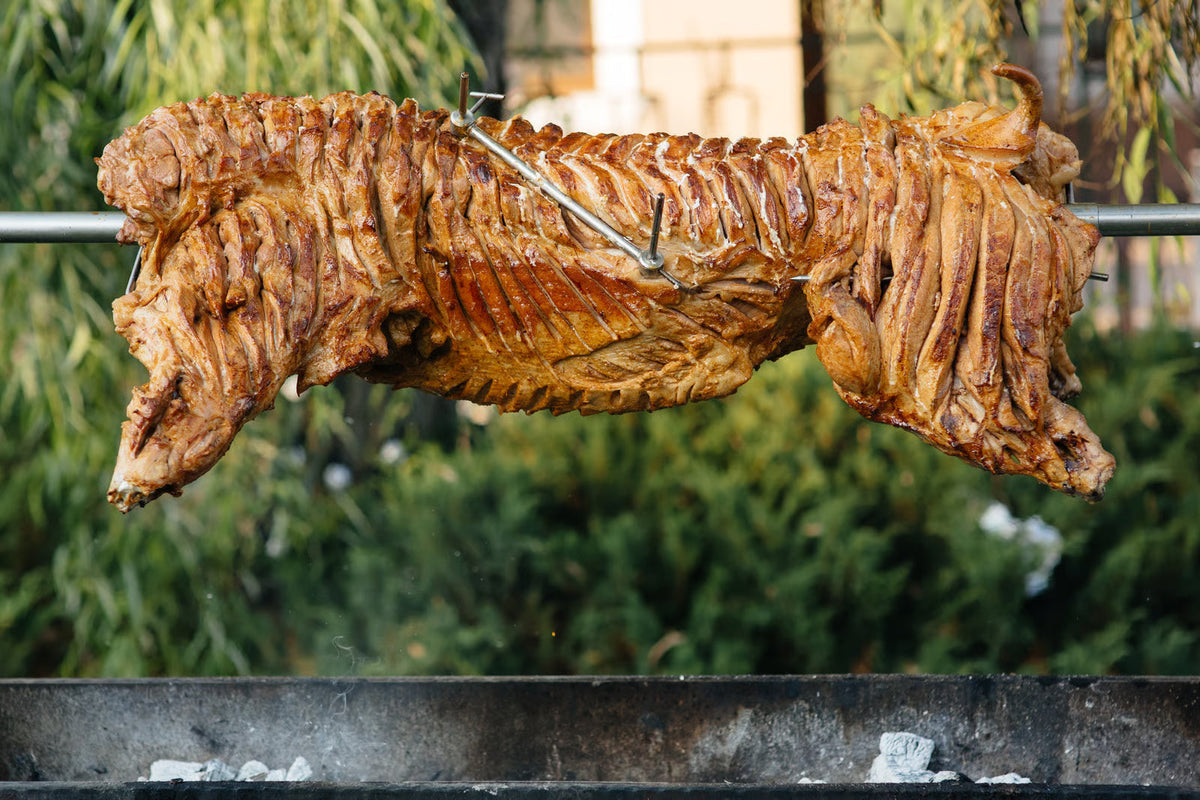 whole lamb rotating on a charcoal spit roaster over glowing embers