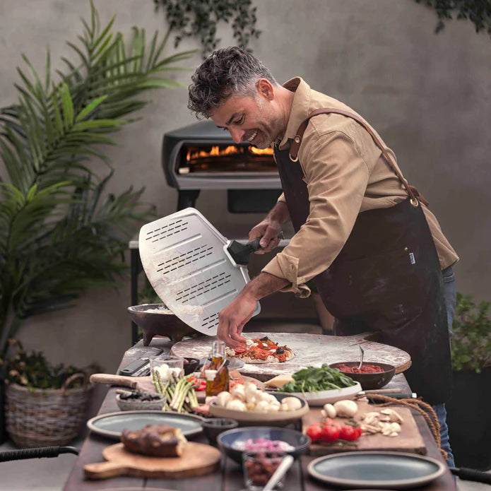 Person using Witt Perforated Pizza Peel 14-inch at outdoor pizza oven
