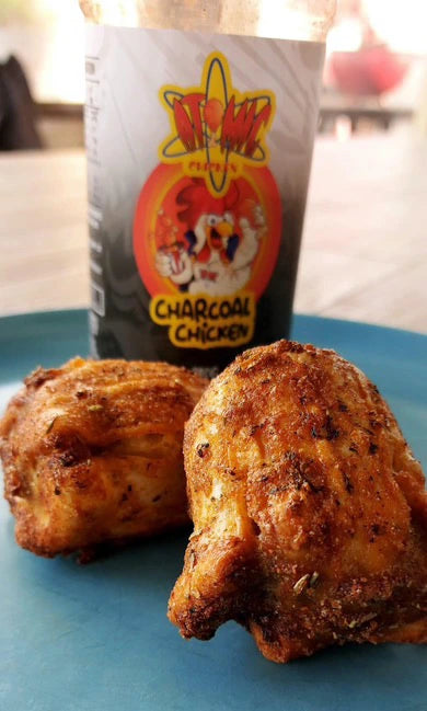 Charcoal-seasoned chicken thighs on a blue plate with Atomic Chicken seasoning jar in the background