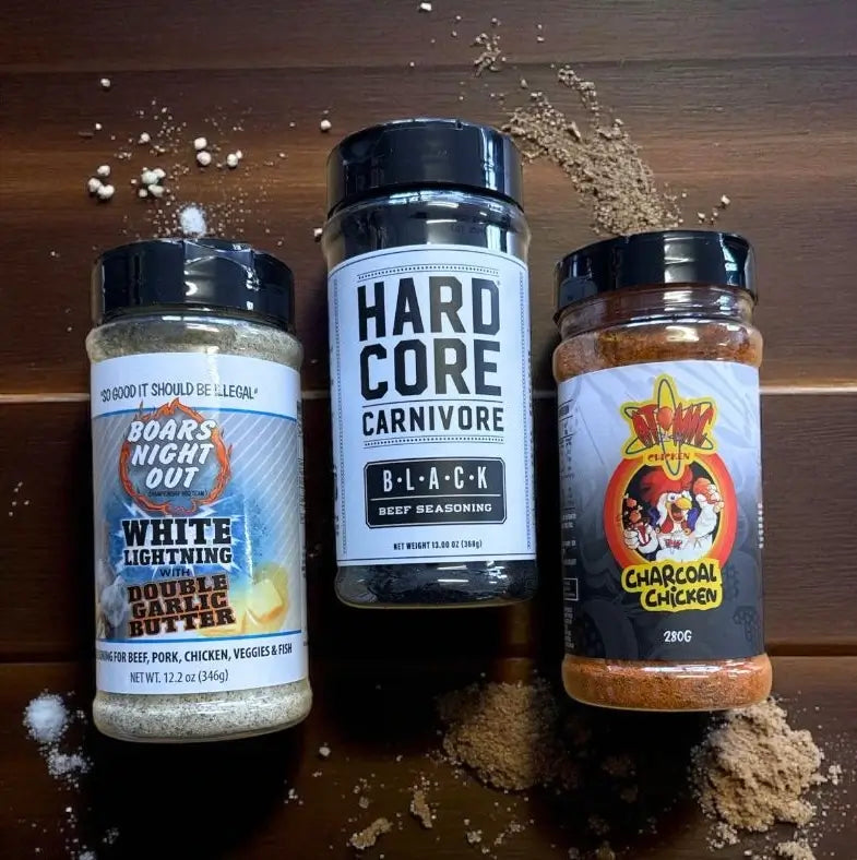 Boars Night Out, Hardcore Carnivore Black, and Charcoal Chicken BBQ rubs on a wooden background with scattered spices