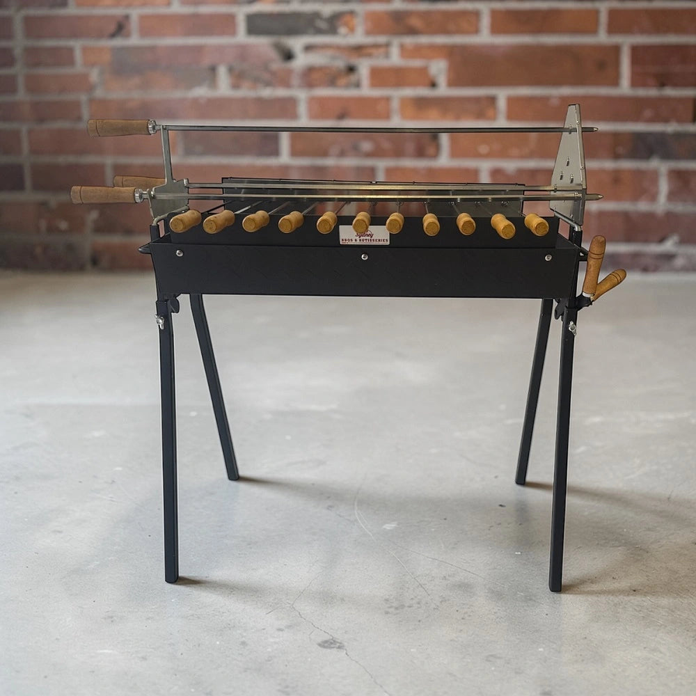 Cypriot souvla BBQ set up outdoors against brick wall with multiple skewers