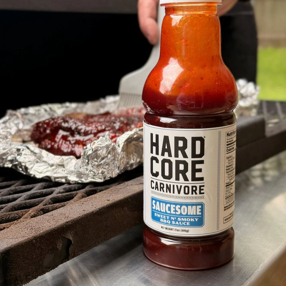 Hardcore Carnivore Saucesome BBQ sauce bottle beside smoker grill