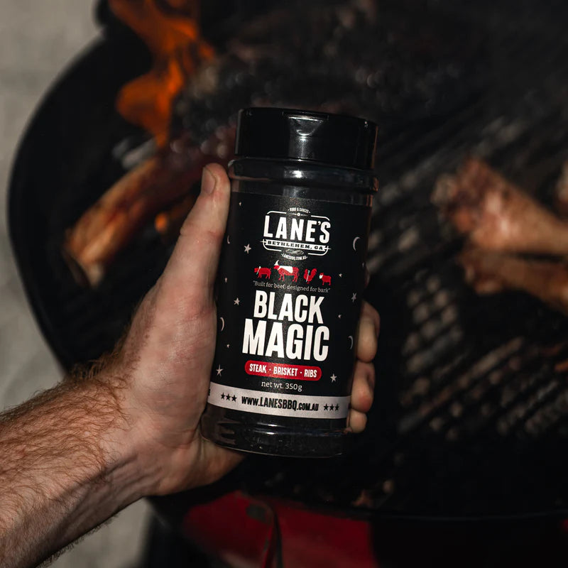 Lane’s Black Magic BBQ rub held near a grill ready for seasoning beef