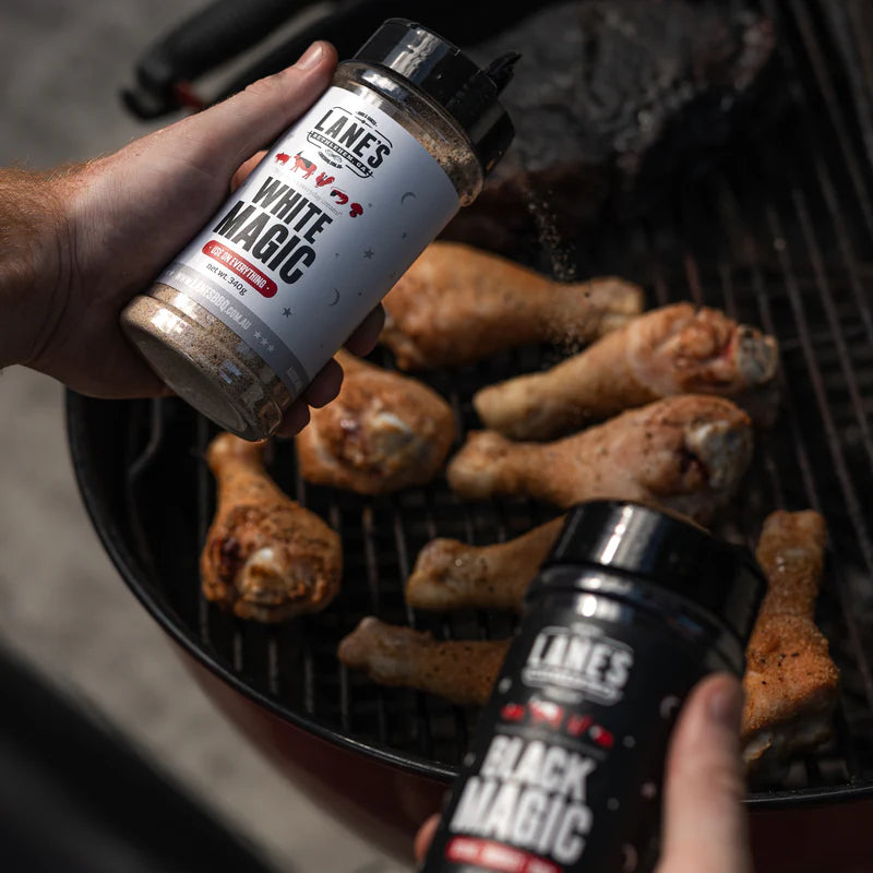 Chicken drumsticks being seasoned with Lane’s Black Magic BBQ rub on a grill