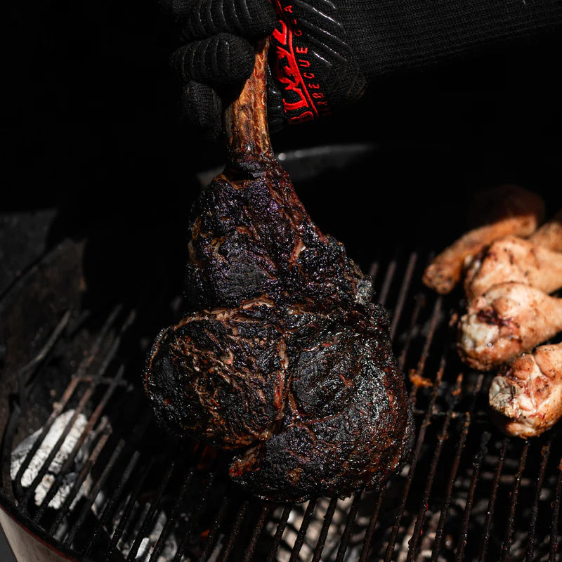 Large tomahawk steak with dark bark cooked over fire using Lane’s Black Magic rub