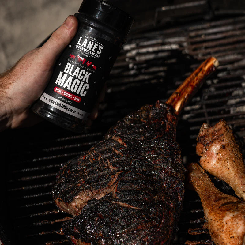 Tomahawk steak coated with Lane’s Black Magic rub cooking over charcoal grill