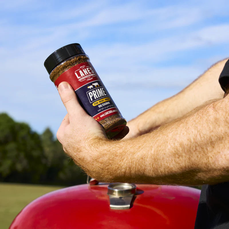 Hand holding Lane’s Prime BBQ rub  over charcoal grill for steak and brisket