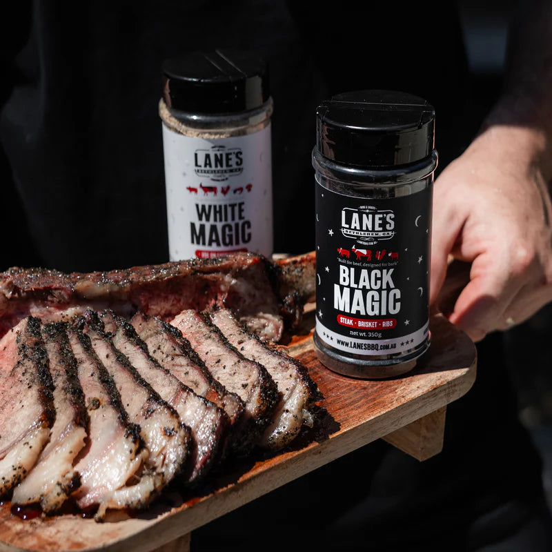 Sliced brisket on a board with Lane’s White Magic and Black Magic BBQ rub bottles