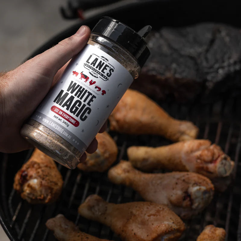 Chicken drumsticks being seasoned with Lane’s White Magic BBQ rub on a grill