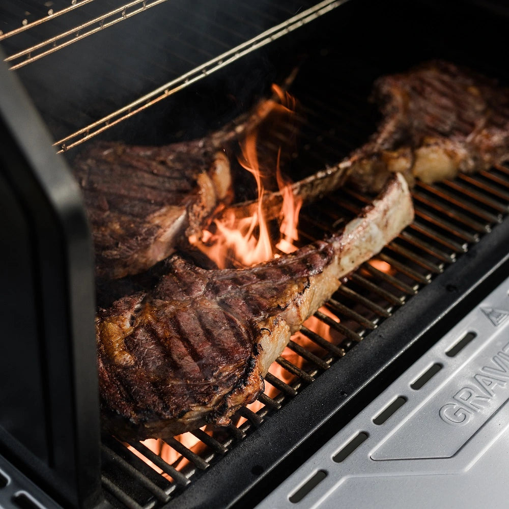 Thick cut steaks searing over an open charcoal flame on the Masterbuilt Gravity Series XT Digital Charcoal BBQ and Smoker with cast iron cooking grates.