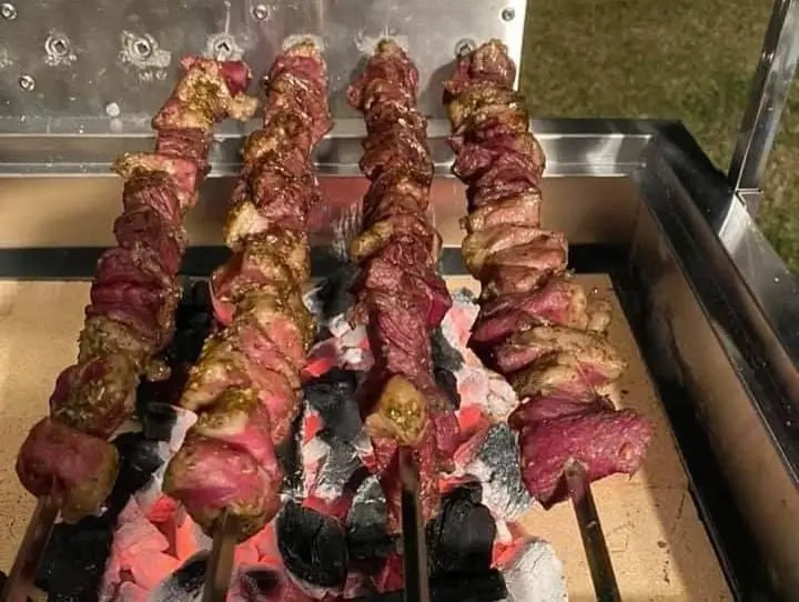 Close-up of small meat skewers cooking on charcoal rotisserie grill